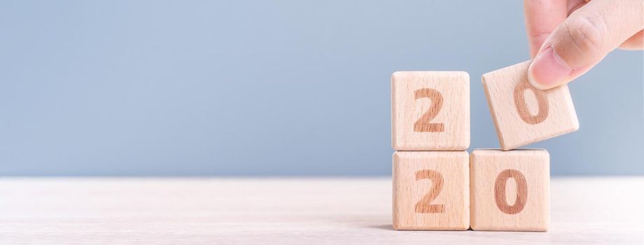 Abstract 2020 & 2019 New year countdown design concept - woman holding wood blocks cubes on wooden table and blue background, close up, copy space.