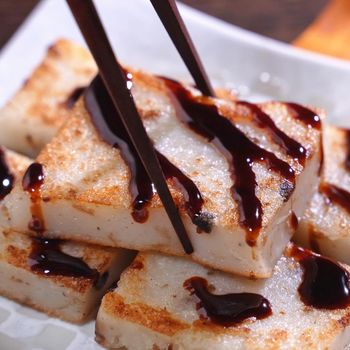 Pouring black soy sauce on ready-to-eat delicious turnip cake, Chinese traditional local dish radish cake in restaurant, close up, copy space.