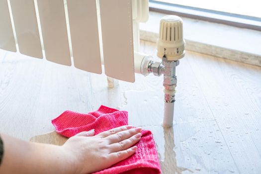 Female hand with rag cleaning water from heating radiator