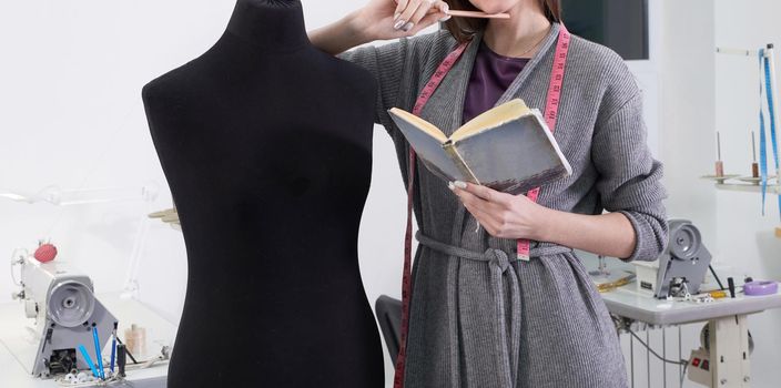 Brunette seamstress in apron measuring beautiful fabric on black dummy in workshop