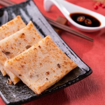 Chinese lunar new year food concept, Delicious turnip radish cake, local cuisine in restaurant with soy sauce on red background, close up, copy space