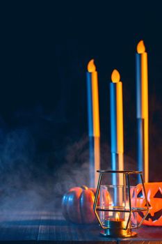 Halloween concept, spooky decorations with lighting up candle and candle holder with blue tone smoke around on a dark wooden table, close up.