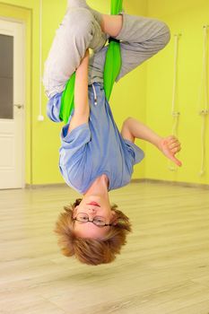 The child is doing yoga in a hammock in the hall. The boy performs asanas in limbo.