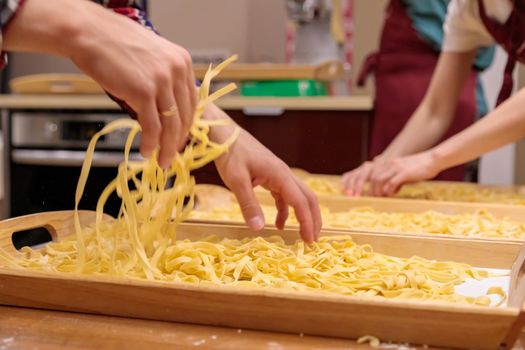The pasta, cut into long strips, lies on a wooden tray. Use your hands to stir the raw pasta for cooking. Close-up.