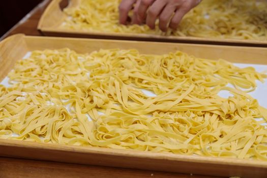 The pasta, cut into long strips, lies on a wooden tray. Use your hands to stir the raw pasta for cooking. Close-up.