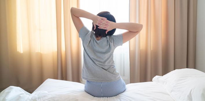 Woman stretching in bed after wake up, back view