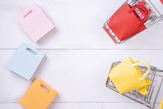 Abstract design element,annual sale,shopping season concept,mini cart with colorful paper bag on white wooden table background,top view,flat lay