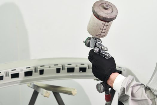 Mechanic painting bumper of a car with sprayer in painting booth