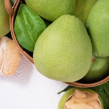 Fresh pomelo, grapefruit in bamboo basket with green leaf on bright white background. Seasonal fruit for Mid-Autumn Festival. Top view. Flat lay.