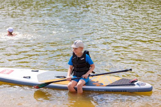 The child is sitting on a surfboard, holding a paddle. Paddleboarding. Russia Zelenograd 14 August 2021