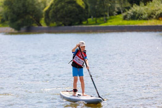 A child swims on a surfboard, pushing off with a paddle. Paddleboarding. Russia Zelenograd 14 August 2021