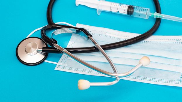 Stethoscope, protective mask and syringe on a blue background close up