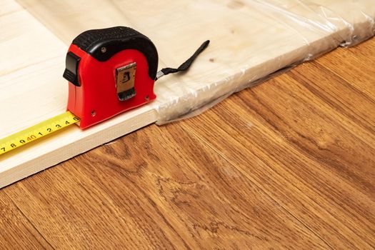 Measuring a wooden board with an yellow tape measure close up, copy space
