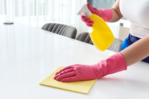 Woman wearing rubber gloves cleaning table with cloth. Disinfecting a kitchen table with bleach