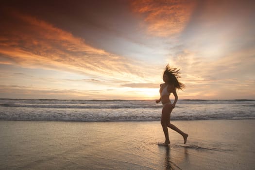 Beautiful sporty girl in bikini run on the seashore at sunset