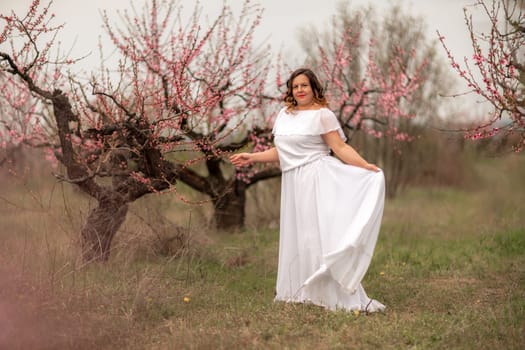 Woman peach blossom. Happy woman in white dress walking in the garden of blossoming peach trees in spring.
