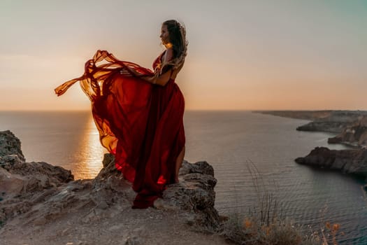 Woman sunset sea red dress, side view a happy beautiful sensual woman in a red long dress posing on a rock high above the sea on sunset