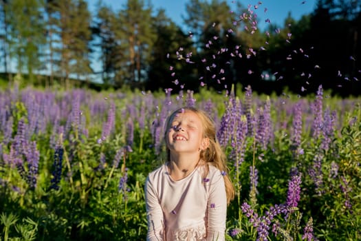 portrait of cute little happy two year old kid girl with bloom flowers lupines in field of purple flowers. nature outdoor.