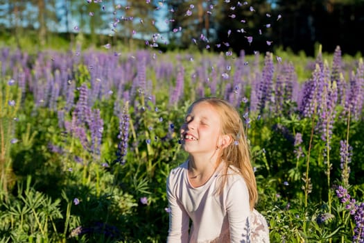 portrait of cute little happy two year old kid girl with bloom flowers lupines in field of purple flowers. nature outdoor.