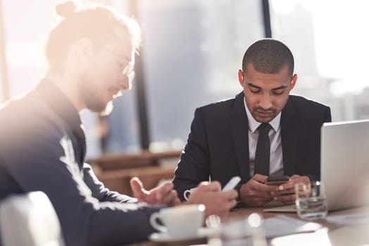 Armed with the smartest technology it takes to be productive. two young businessmen using their smartphones at work