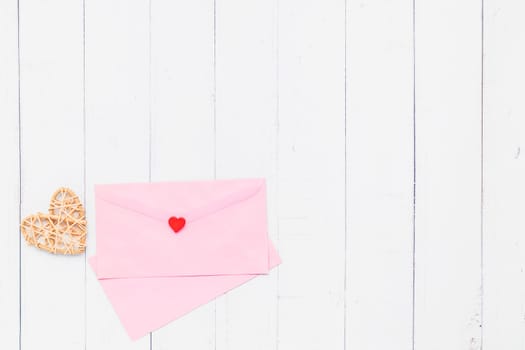 Flat lay of pink envelope with wooden wicker heart on white table background for love and Valentine's day concept