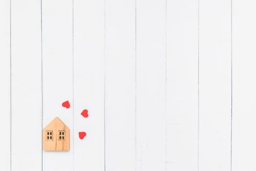 Flat lay of the wooden house model with red heart on white table background for family and love concept