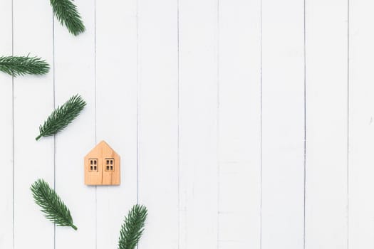 Flat lay of the wooden house model with fir tree branches on white table background for family and Christmas decoration concept