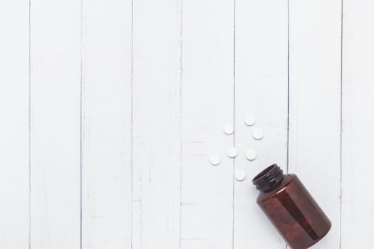 Flat lay of piles of pills were released from the brown bottle on white table background for medical and healthcare concept