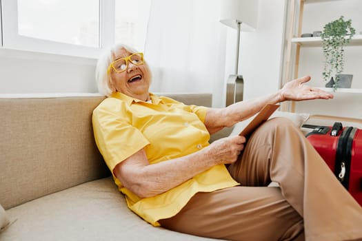 Happy senior woman with passport and travel ticket packed a red suitcase, vacation and health care. Smiling old woman joyfully sitting on the sofa before the trip raised her hands up in joy. High quality photo