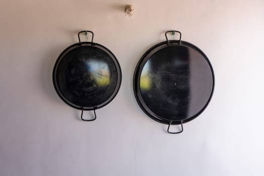 Paella pans hanging on the white wall, utensil for paellas, traditional Spanish food.