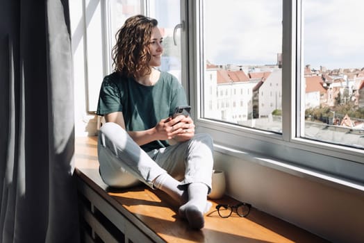 Digital Detox: Serene Young Woman Embracing Relaxation at Home, Gazing out of Window, Disconnecting from Technology in a Peaceful Lockdown Retreat