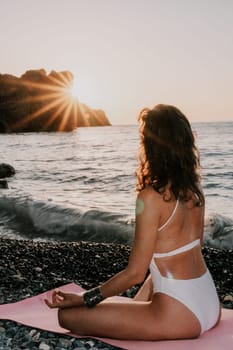 Young woman in swimsuit with long hair practicing stretching outdoors on yoga mat by the sea on a sunny day. Women's yoga fitness pilates routine. Healthy lifestyle, harmony and meditation concept.