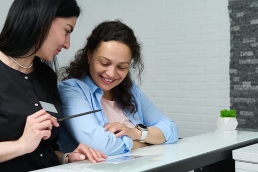 Confident young female doctor talking to her patient, expianing treatment, prescribing medicines, standing at the reception counter in a modern clinic or outpatient hospital. Healthcare and medicine