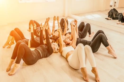 Group of young womans fitness instructor in Sportswear Leggings and Tops, stretching in the gym before pilates, on a yoga mat near the large window on a sunny day, female fitness yoga routine concept.