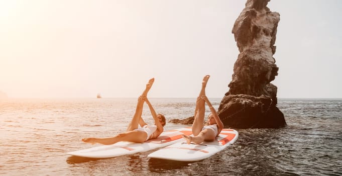 Woman sup yoga. Middle age sporty woman practising yoga pilates on paddle sup surfboard. Female stretching doing workout on sea water. Modern individual hipster outdoor summer sport activity