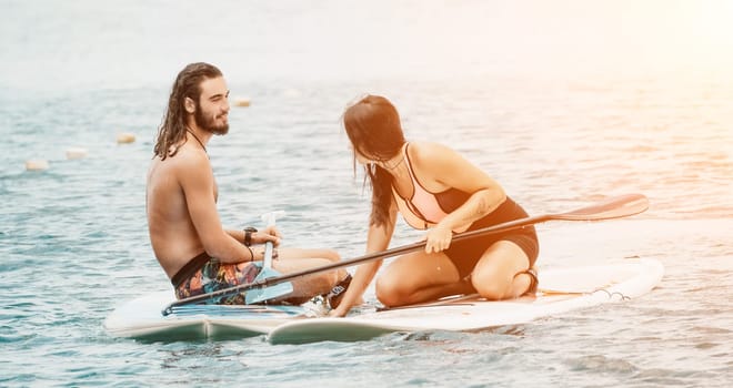 Sea woman and man on sup. Silhouette of happy young woman and man, surfing on SUP board, confident paddling through water surface. Idyllic sunset. Active lifestyle at sea or river