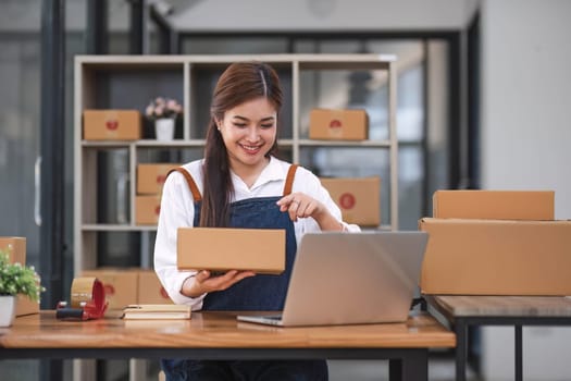 Startup happy Asian woman business owner works with a box at home office. prepare parcel delivery SME supply chain, procurement, package box to deliver to customers, Online SME business entrepreneurs ideas