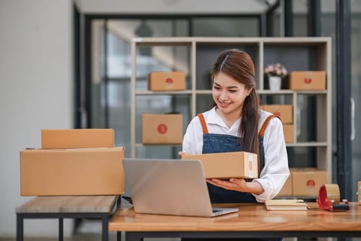 Startup happy Asian woman business owner works with a box at home office. prepare parcel delivery SME supply chain, procurement, package box to deliver to customers, Online SME business entrepreneurs ideas