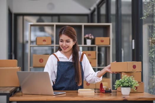 Startup happy Asian woman business owner works with a box at home office. prepare parcel delivery SME supply chain, procurement, package box to deliver to customers, Online SME business entrepreneurs ideas