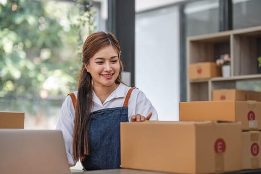 Startup happy Asian woman business owner works with a box at home office. prepare parcel delivery SME supply chain, procurement, package box to deliver to customers, Online SME business entrepreneurs ideas