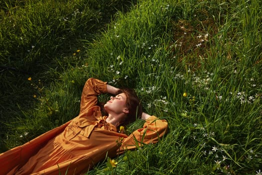 a happy, relaxed woman, resting lying in the green grass, in a long orange dress, with her eyes closed and a pleasant smile on her face, enjoying harmony with nature and recuperating. High quality photo