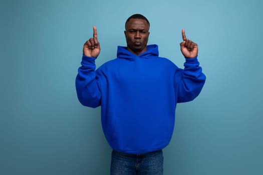 energetic positive young african man consultant in stylish hoodie shows with hand actual offer on studio background with copy space.