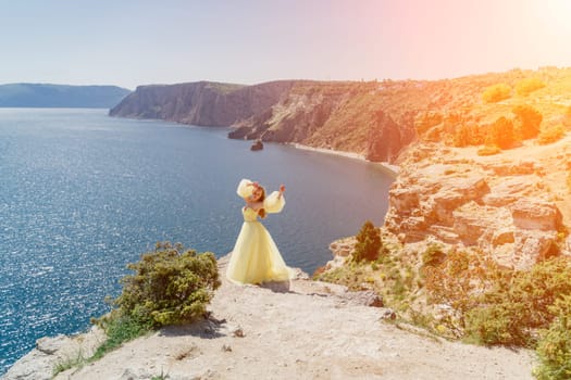 Woman yellow dress sea. Side view Young beautiful sensual woman in yellow long dress posing on a rock high above the sea at sunset. Girl in nature against the blue sky.