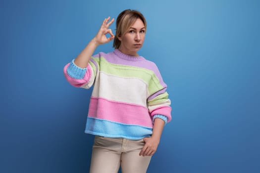 serious blond young woman in a striped sweater shows with her hand a class in on a blue background.