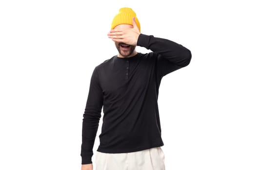 shy young 30 year old guy with a beard dressed in a black jacket and a yellow hat.
