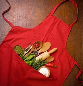 Baking background with red apron, rolling pin, herbs and kitchen utensils on a black background. View from above. Flat style.