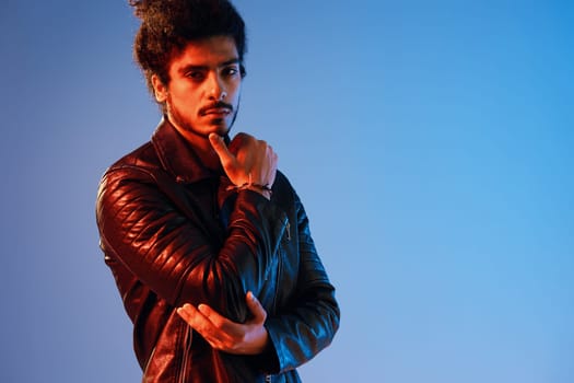 Portrait of a stylish man with curly hair on a blue background multinational, colored light, black leather jacket trend, modern concept. High quality photo