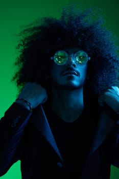 Fashion portrait of a man with curly hair on a green background with sunglasses, multinational, colored pink light, trendy, modern concept. High quality photo