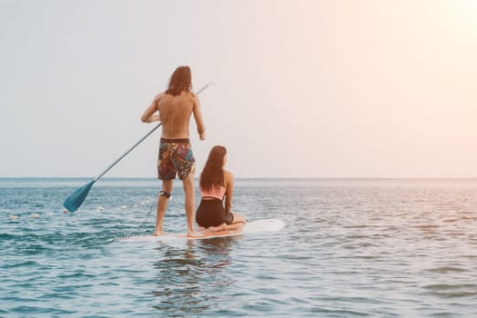 Sea woman and man on sup. Silhouette of happy young woman and man, surfing on SUP board, confident paddling through water surface. Idyllic sunset. Active lifestyle at sea or river