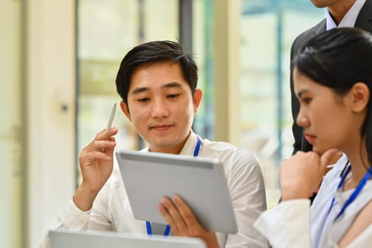 Focused business team looking at digital tablet screen, brainstorming for important project in modern corporate office.